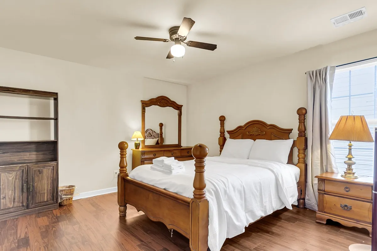 A peaceful bedroom with a comfortable bed, nightstand and lamp, mirror, and bookshelf. The space feels serene and private, perfect for rest or quiet activities like reading.