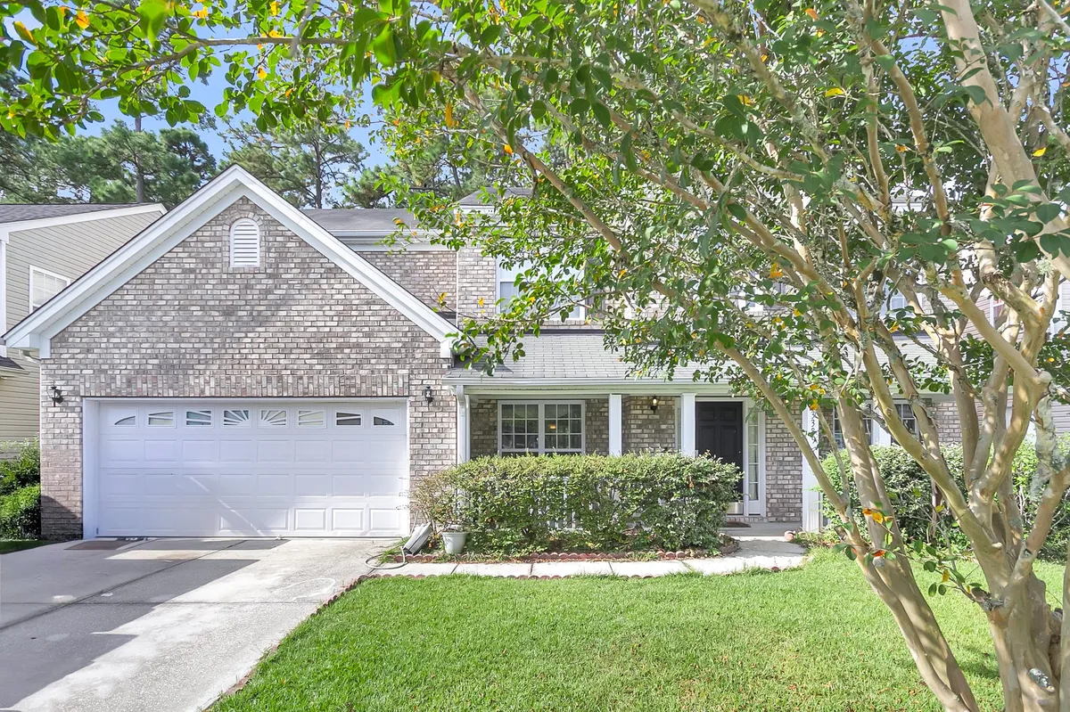 This image features the home's brick facade, a welcoming front porch adorned with comfortable seating, a lush green lawn, and mature trees surrounding the property. The setting evokes a sense of security and an inviting space for family gatherings, outdoor play, or relaxing mornings on the porch.