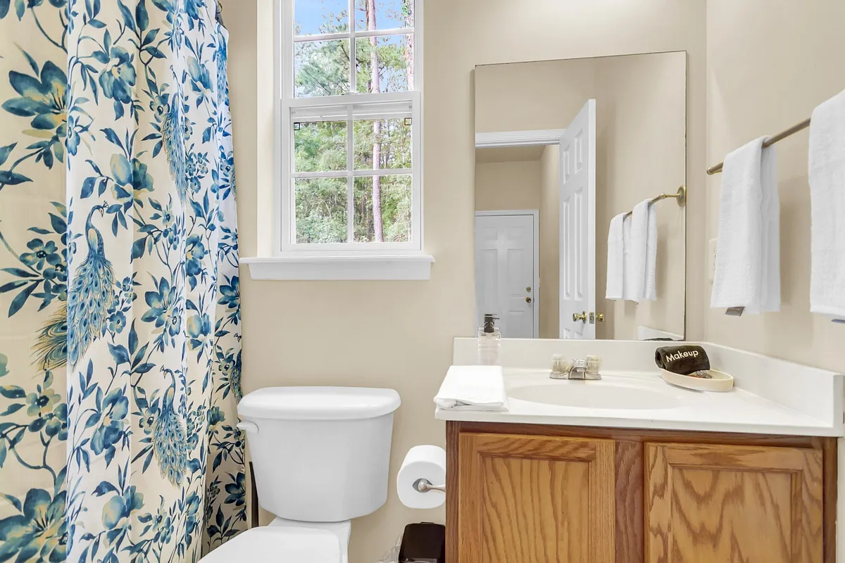 A serene bathroom with a floral shower curtain, vanity with mirror, and a window that lets in natural light. The space feels inviting and fresh, ideal for morning routines or relaxing baths.