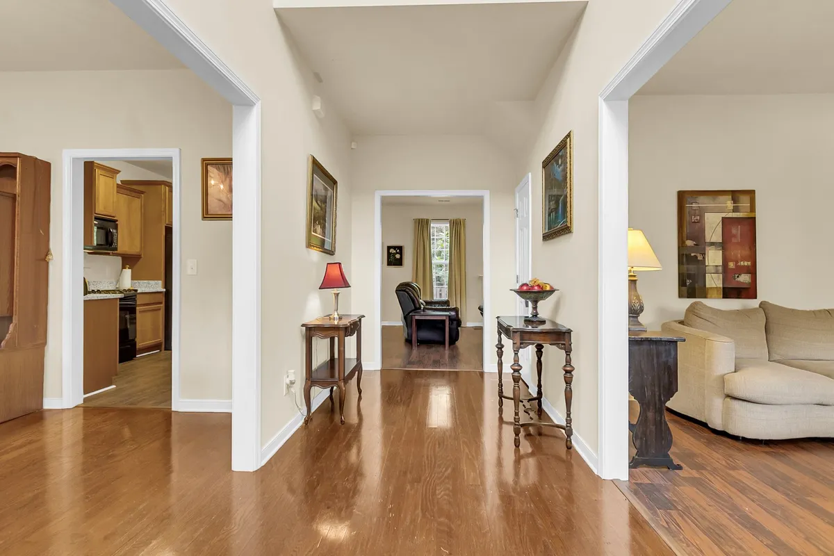 Featuring an entrance hallway with a table and lamp, a glimpse of a cozy sofa, and art displayed on the walls, the image presents a thoughtfully organized passageway leading from the entry into the rest of the home. The warm lighting and tasteful decor evoke a sense of welcome and order.
