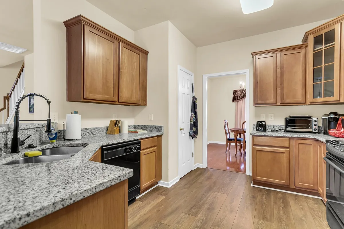 This image features a well-equipped kitchen with granite countertops, wood cabinets, stainless steel appliances, and a view into the adjoining dining area. The open sight lines between kitchen and dining space emphasize the open-concept layout and facilitate easy flow for both meal prep and socializing.