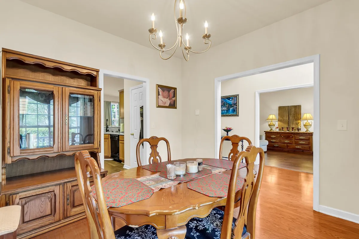 A cozy dining area is the focal point, featuring a sizable dining table beneath a chandelier, a wooden cabinet for storage, and artwork adorning the wall. The warm, inviting mood makes it ideal for family gatherings and dinner parties.